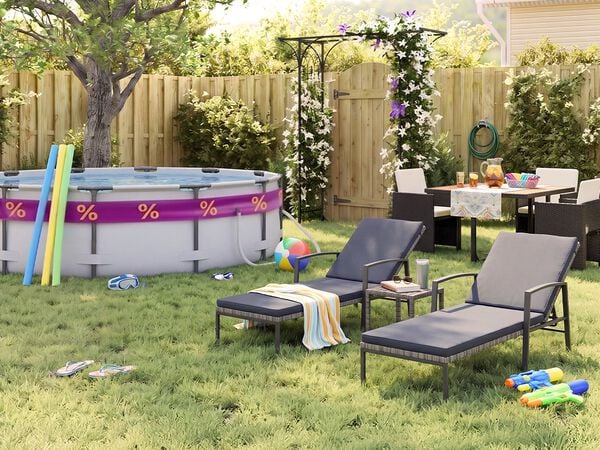Sunny backyard garden with an above-ground swimming pool, pool noodles, goggles, beach ball, and flip-flops on the grass. Two black metal sun loungers with grey cushions sit beside a small side table, while an outdoor dining set with dark rattan chairs is arranged near a flowering pergola, wooden fence, garden plants, and summer party accessories.