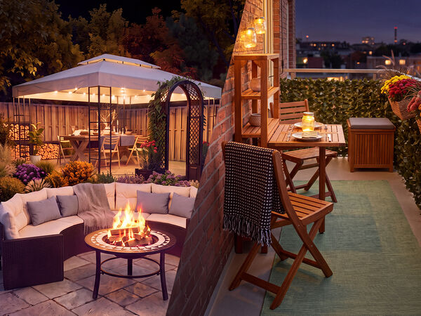 Cozy outdoor living spaces at dusk, featuring a garden lounge set with a fire pit and a flower-filled gazebo on one side, and a decorated balcony with wooden furniture, lantern lighting, and potted flowers overlooking a city skyline on the other.