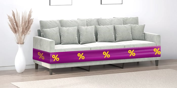 Grey three-seater sofa with cushions and purple ribbon showing discount icons, in a styled living room. Click to shop the products in the offer.