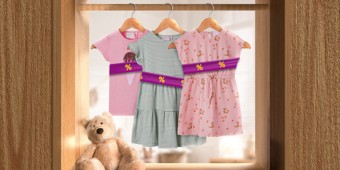 Kids' clothes on hangers wrapped in a purple promotional band with yellow discount icons, hanging on a rail indoors. Click to see the products in the offer.